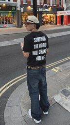 Person wearing a black t-shirt with text on the back, standing on a city street.